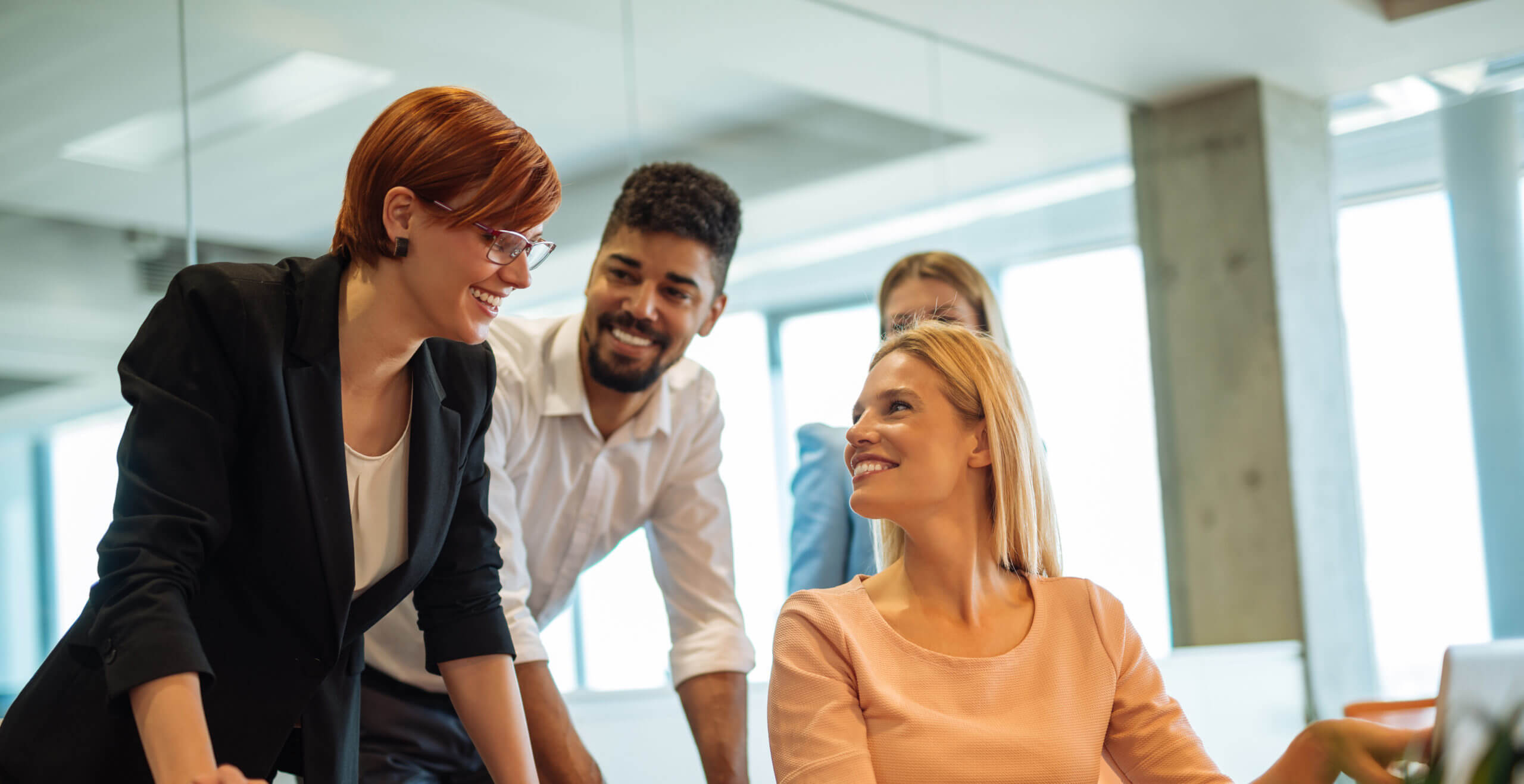 Businesspeople standing around woman sitting pointing at laptop and smiling