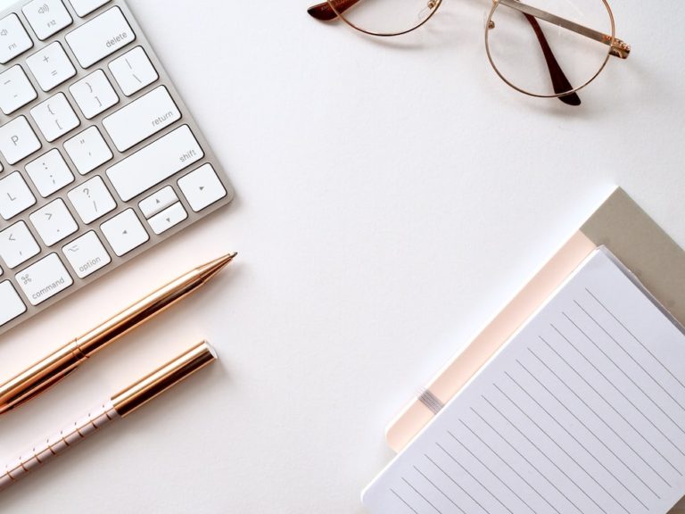 Tidy desk with notepad, glasses and keyboard on